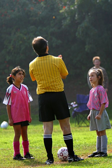 Maryam and an Angel watch as referee José flips a coin to start the game